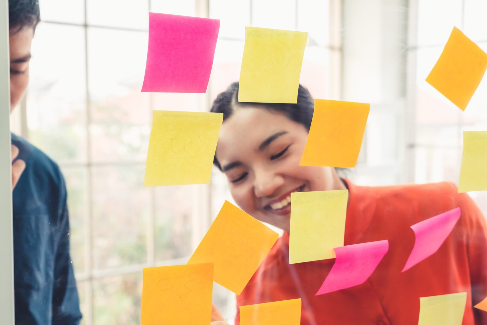 Business people work on project planning board in office and having conversation with coworker friend to analyze project development . They use sticky notes posted on glass wall to make it organized .